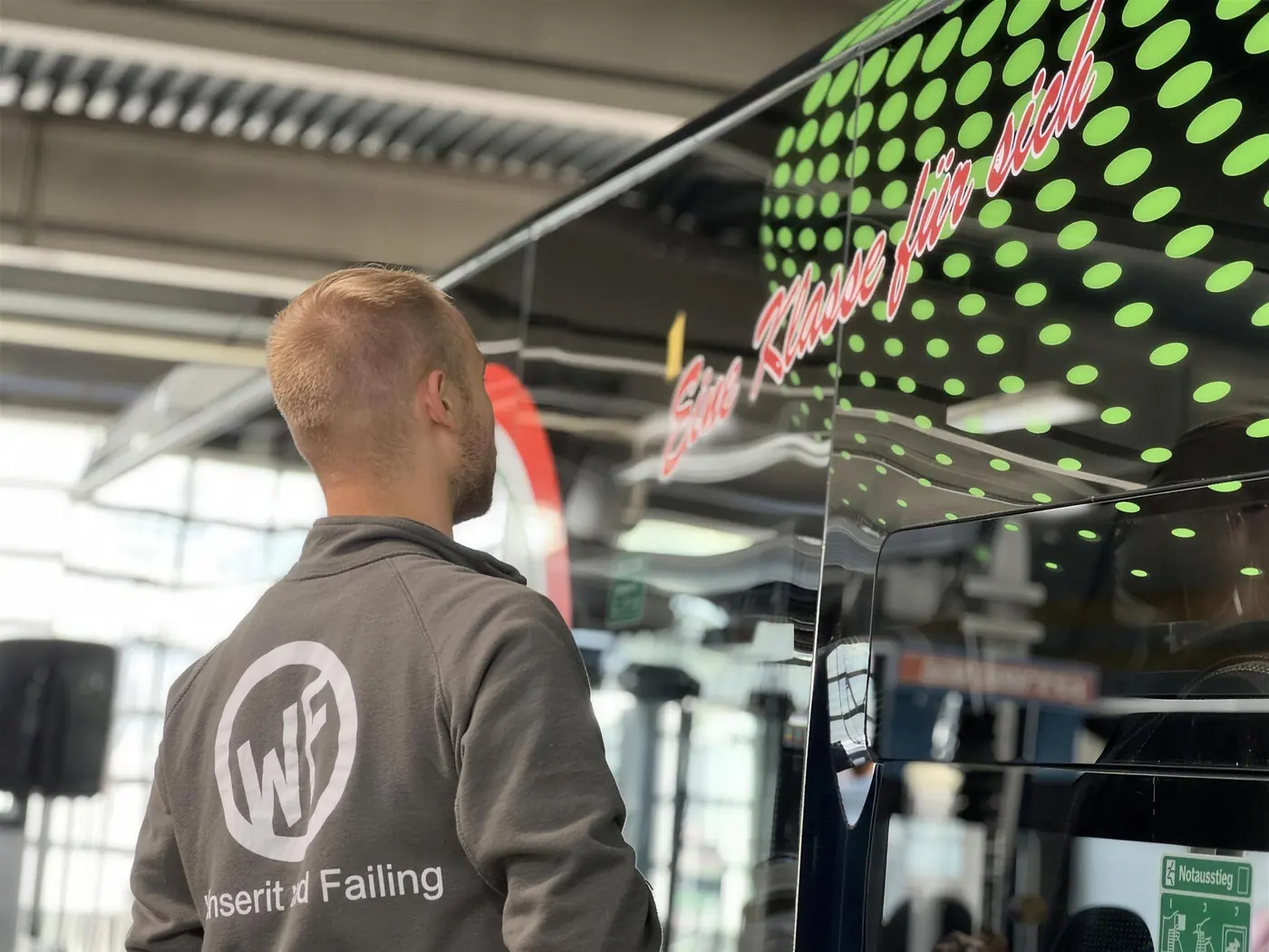 WF Design Monteur mit Firmenpullover bei der Beschriftung eines Busses